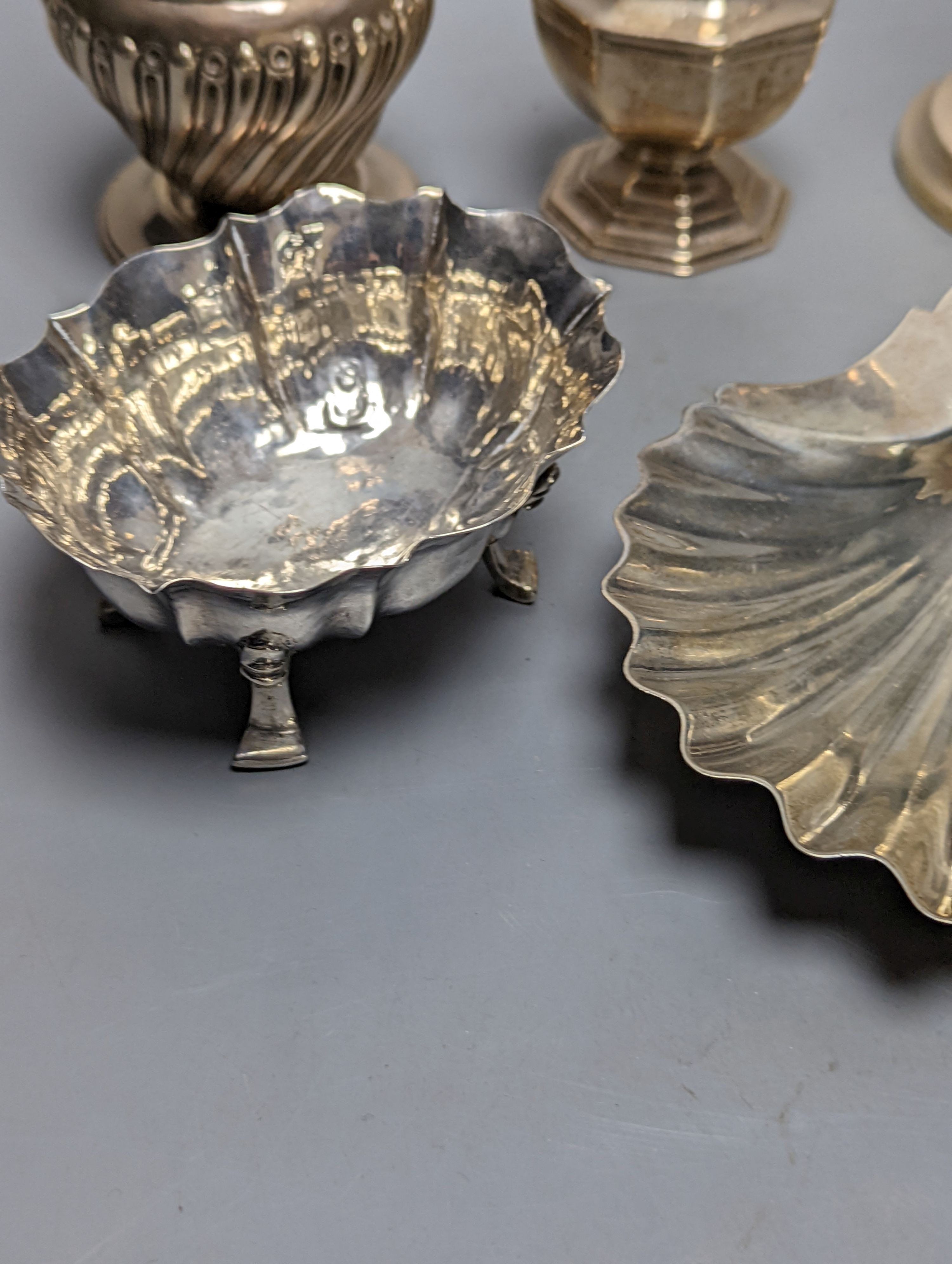A mixed collection of silver to include a George III silver butter shell, London, 1799, a small cigarette box, two casters, a pair of slender candlesticks (loaded) and two small bowls including white metal